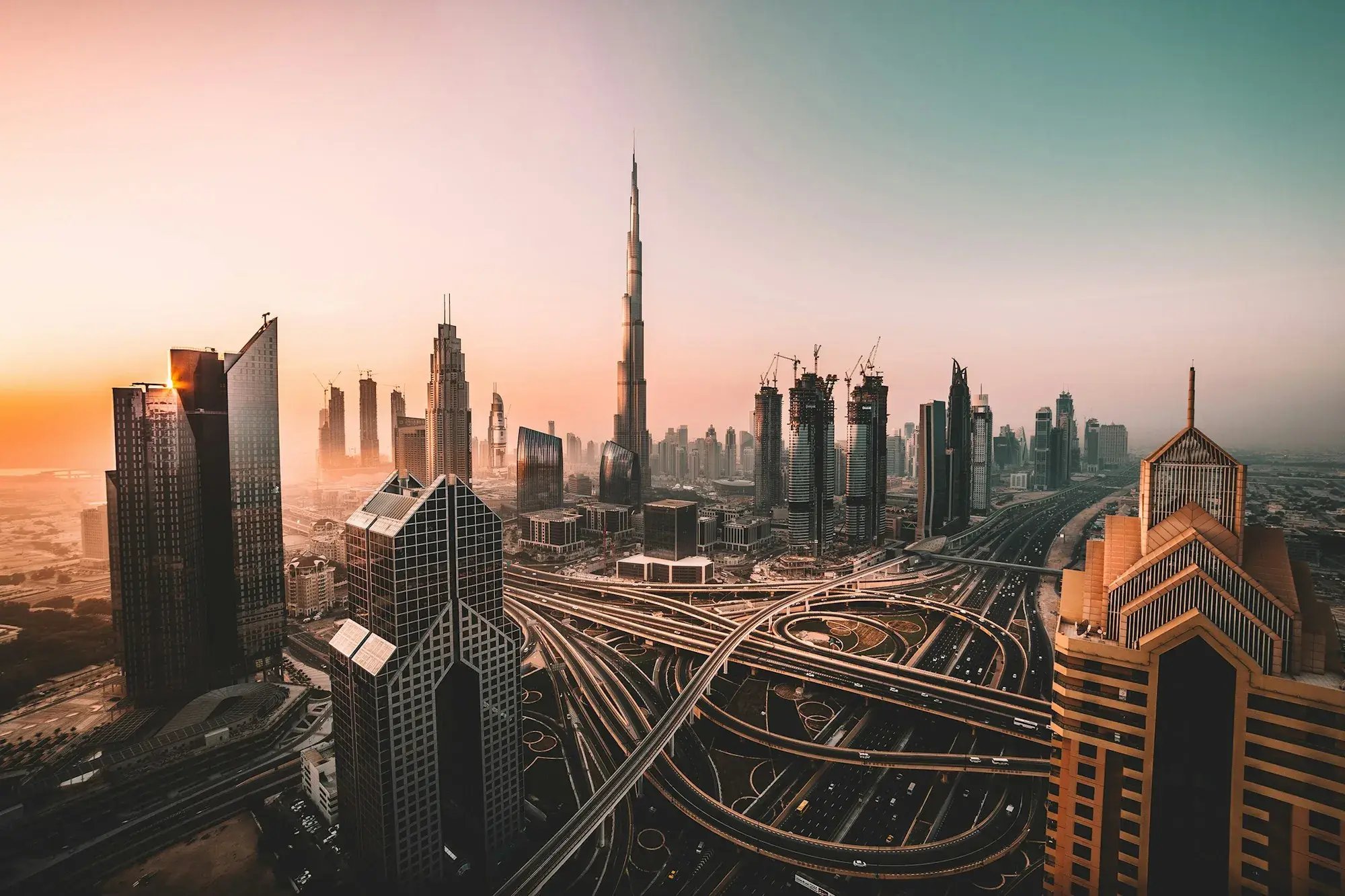 The Burj Khalifa and Downtown Dubai skyline above a multi-level highway interchange at sunset